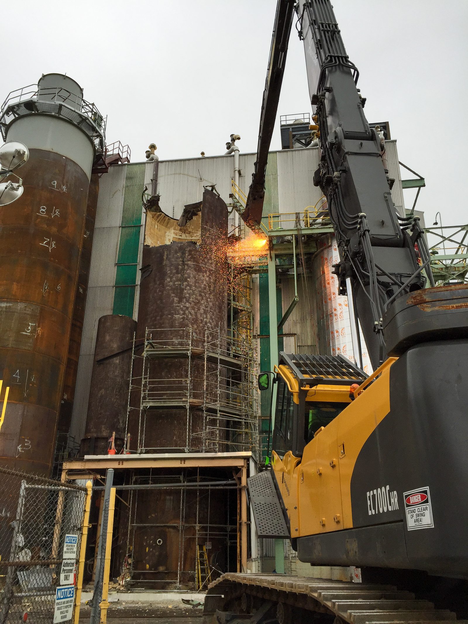 Excavator with shear removing the steel Pine DO tank beside the operating bleach plant